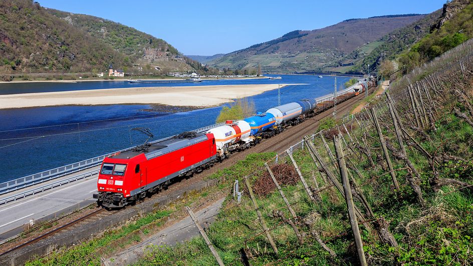 Un train de marchandises de DB Cargo sur la ligne du Rhin ; à l'arrière-plan, on aperçoit le Rhin dont le niveau est bas.