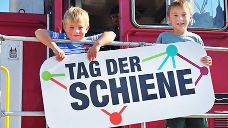 Des enfants se tiennent debout sur une locomotive et tiennent ensemble une affiche de la « Journée du rail »